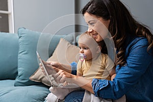 Mother, baby and tablet on sofa watching educational video online on streaming service in home. Love, family time and woman with