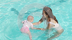 Mother and baby together at pool. Mom supporting infant child at swimming pool water.