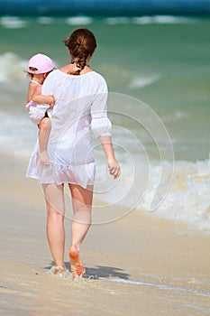 Mother and baby walking along tropical beach