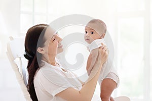 Mother and baby in white bedroom. Asian mom