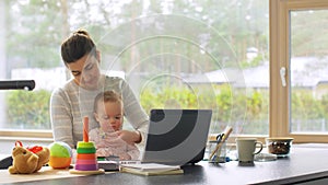 Mother with baby working on laptop at home office