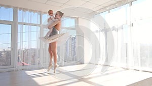 Mother in ballet outfit standing on tiptoe and holding on hands small daughter