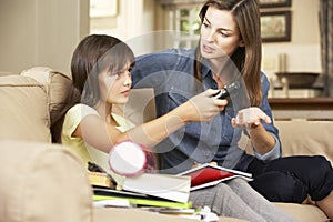 Mother Becoming Frustrated As Daughter Watches TV Whilst Doing Homework Sitting On Sofa At Home