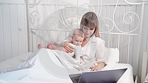 Mother in bed with baby working with computer.
