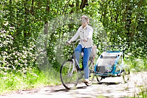 Mother on bicycle with baby bike trailer in park