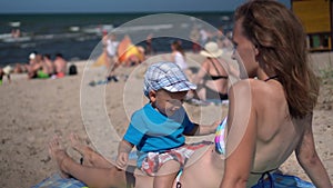 Mother in bikini with little son on her stomach lying on beach