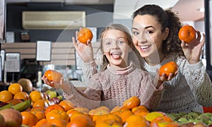 Mother and blonde daughter buying mandarins in shop