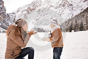 Mother blowing snow on child among snow-capped mountains