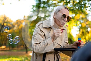 Mother blows soap bubbles to entertain baby in stroller.