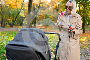 Mother blows soap bubbles to entertain baby in stroller.