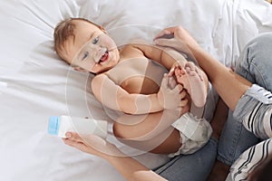 Mother with bottle of dusting powder near her cute baby on bed, top view