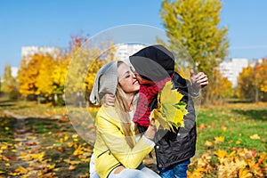 Mother and boy walking in autumn park. The child gently hugs and kisses mom.