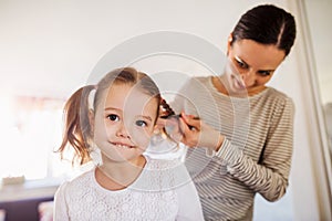 Mother braiding hair of her daughter in the morning