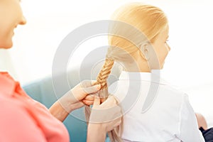 The mother braids her daughter`s hair. A woman plaits a braid a little girl.