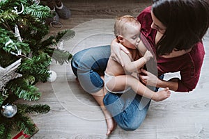 mother breastfeeding her baby girl by the Christmas tree