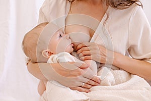 Mother is breastfeeding her baby. Woman in white and child on her arms. Kid sucks breast milk.