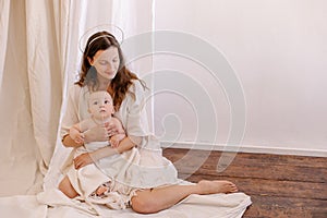 Mother is breastfeeding her baby. Woman in white and child on her arms. Kid sucks breast milk.