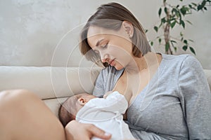 A Mother breastfeeding her little baby boy in her arms. white sofa, home, white top