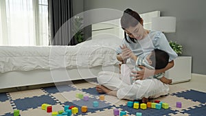 mother breastfeeding infant baby after playing wooden block in bedroom