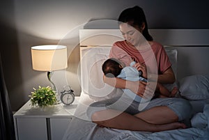 mother breastfeeding newborm baby on bed at night