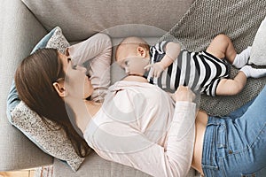 Mother breastfeeding newborn baby lying on sofa at home