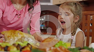 Mother brings baked chicken dish from oven at family thanksgiving birthday celebration in kitchen. Little girl sniffs