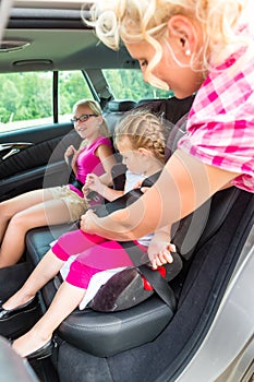 Mother buckling up on child in car photo