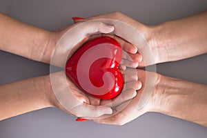 Mother care or love concept with child and mom hands holding a red heart shape