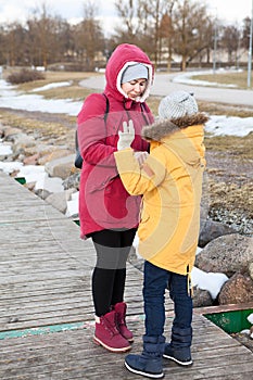 Mother cares for her presteen daughter in the frosty air, people wearing down jackets walk on winter street