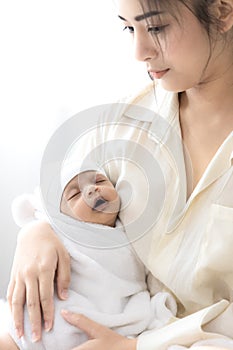 Mother carrying her baby in white bed room. Cute newborn baby sleeping in mother `s arm. Housewife and mother `s day concept