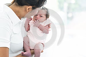 Mother carrying and kissing her newborn baby girl at home. Cute 19 days Asian Australian infant baby lean in mom arms. Parent and
