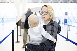 Mother carying his infant baby boy child queuing at airport terminal in passport control line at immigrations departure photo