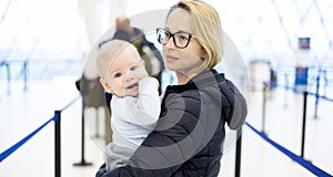 Mother carying his infant baby boy child queuing at airport terminal in passport control line at immigrations departure photo