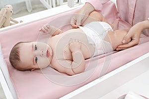 Mother changing baby`s diaper on table at home