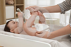 Mother changing baby`s diaper on table at home, closeup