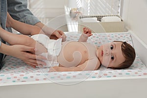 Mother changing baby`s diaper on table at home, closeup