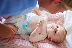 Mother Changing Baby Son's Nappy As He Lies On Mat