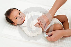 mother changing diaper of newborn baby while lying on bed