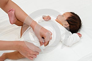 mother changing diaper of newborn baby while lying on bed