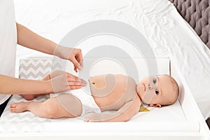 Mother changing her baby`s diaper on table