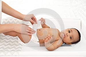 Mother changing her baby`s diaper on table