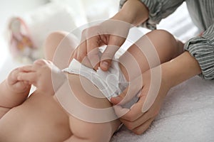 Mother changing her baby`s diaper on table