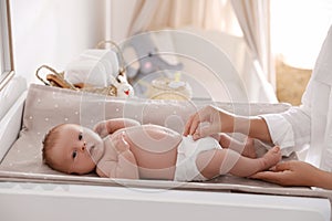 Mother changing her baby`s diaper on table