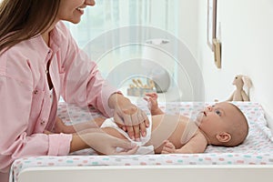 Mother changing her baby`s diaper on table at home