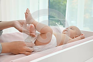 Mother changing her baby`s diaper on table at home