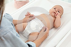 Mother changing her baby`s diaper on table at home