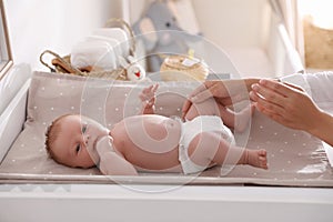 Mother changing her baby`s diaper on table in room