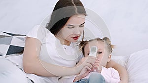 Mother is checking her daughter's temperature laying on bed