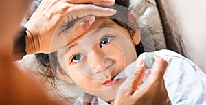 Mother checking temperature of her sick daughter with thermometer in mouth