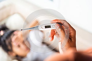 Mother checking temperature of her sick daughter with thermometer in mouth